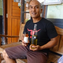 Master beekeeper, Made Yustika sitting with a jar of honey and bottle of Arak