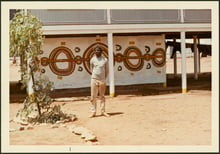 Mural on the side of a building with the artist standing in front.
