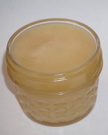 A small faceted glass jar filled to the rim with pale ivory creamed honey, seen from above on a white surface.
