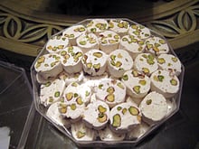 Round white pieces of soft nougat studded with green pistachios, arranged in a clear octagonal tray.