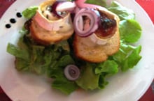 A plate of goat cheese toasts topped with honey and red onion rings on a bed of lettuce.
