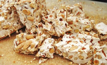 Broken chunks of white nougat packed with whole almonds on a board scattered with crumbs.