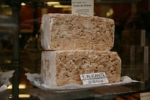 Two tall blocks of hard white nougat packed with whole almonds in a shop window, with a card reading Turrón de Alicante.