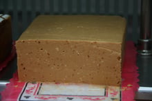 A single smooth block of soft, light-brown almond paste nougat on a red paper doily.