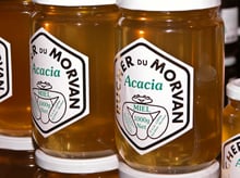 Glass jars of pale golden honey with hexagonal labels reading Rucher du Morvan, Acacia, Miel 1000 g.