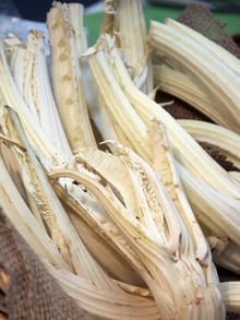 A pile of long, curved, cream-white cardoon stalks on hessian sacking.