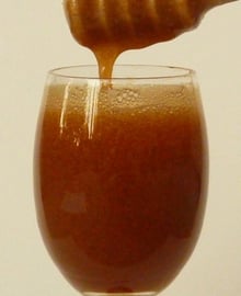 Amber-brown honey running from a wooden dipper into a stemmed glass filled with the same honey.