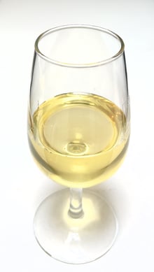 Pale yellow, clear liquid honey in a stemmed tasting glass on a white surface.