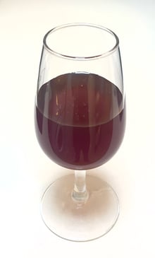 A stemmed tasting glass half filled with dark red-brown honey against a white background.
