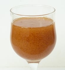 A stemmed tasting glass filled with orange-brown honey, grainy with fine crystals, against a white background.