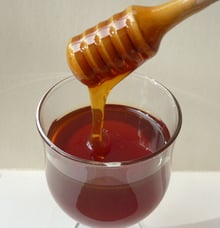 Dark reddish-amber honey falling in a ribbon from a wooden dipper into a clear tulip glass.