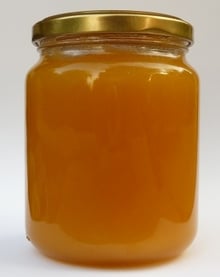 A full glass jar of thick honey with a gold screw lid against a white background.