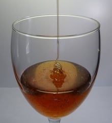 Amber honey falling in a thin stream into a stemmed wine glass.