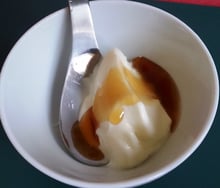 A white bowl of thick yogurt with golden honey poured over it and a spoon.
