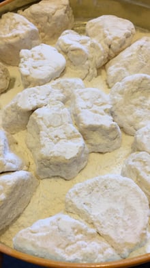 Lumps of pale, soft confection half-buried in white powder on a round metal tray.