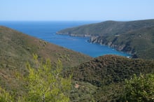 Scrub-covered hills running down to a blue bay, with a headland beyond.