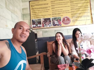 Madi sitting with two women under a sign in Indonesian.