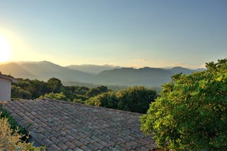 Scrub-covered ridges receding into haze at sunset, seen over a tiled roof.