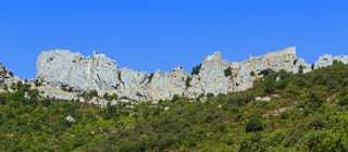 A long ruined fortress following the top of a narrow limestone ridge, its walls and towers running the whole length of the crest above wooded slopes.
