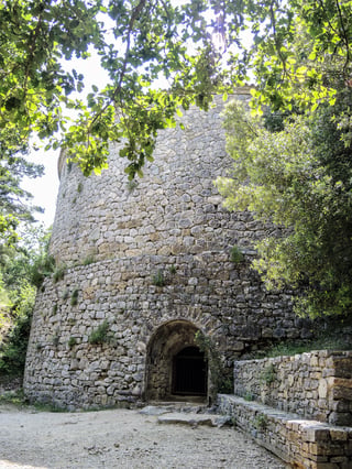 A tall circular drystone ice tower seen from its foot, the coursed stonework filling the frame against trees and sky.