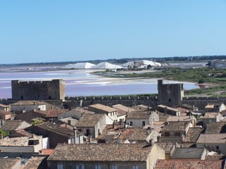 Salt pans with pink-tinted water, white conical mountains of harvested salt beside them, and the medieval ramparts of Aigues-Mortes on the skyline.
