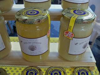 Large glass jars of pale yellow honey with lavender labels and a red Label Rouge sticker on a market stall.