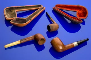 Three wooden tobacco pipes and two open fitted cases on a blue background.