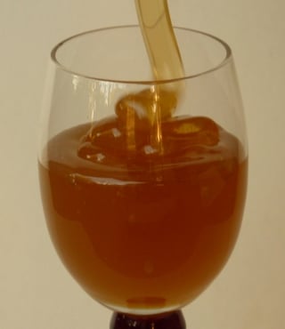 Light gold honey ribboning down and coiling into a clear stemmed glass half full of honey.