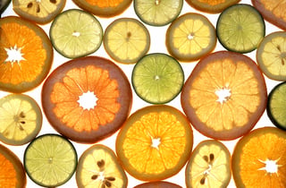 Backlit slices of orange, pink grapefruit, yellow lemon and green lime laid out on a white light table.