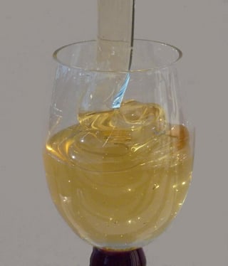 Pale gold honey folding in ribbons from a glass rod into a stemmed tasting glass.
