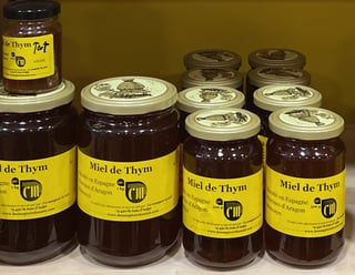 Four glass jars and a small tester of dark amber honey with yellow labels reading Miel de Thym.