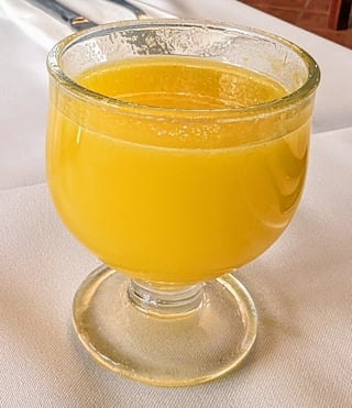 A short stemmed glass filled with cloudy yellow drink standing on a white tablecloth.