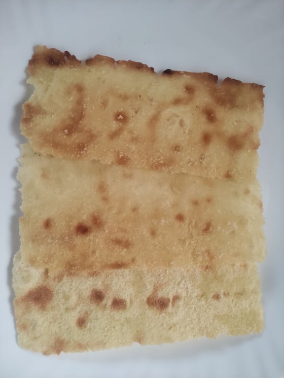 Three thin sheets of crisp flatbread with brown baking spots, overlapping on a white surface.