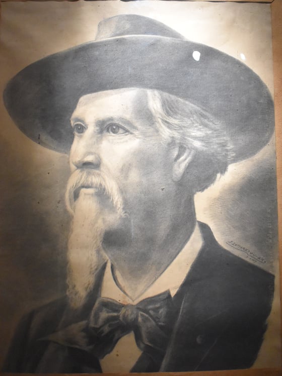 Charcoal drawing of an old man with a long white goatee and moustache under a broad-brimmed felt hat, in a dark coat and bow tie.