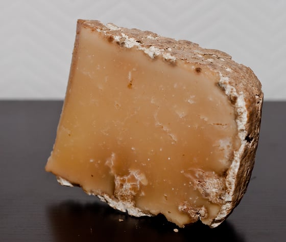 A wedge of hard cheese with an amber, glassy interior and a thick grey-brown natural rind.