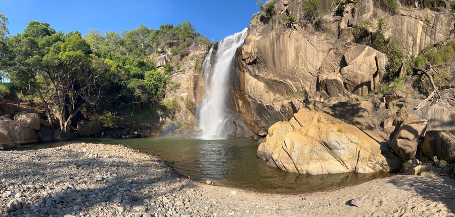 A waterfall flanked by trees on the left and a rock face on the right. A small pond in front