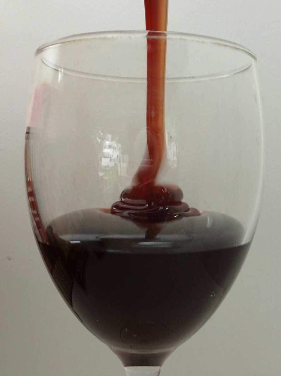 A wine glass half full with dark honey pouring in.