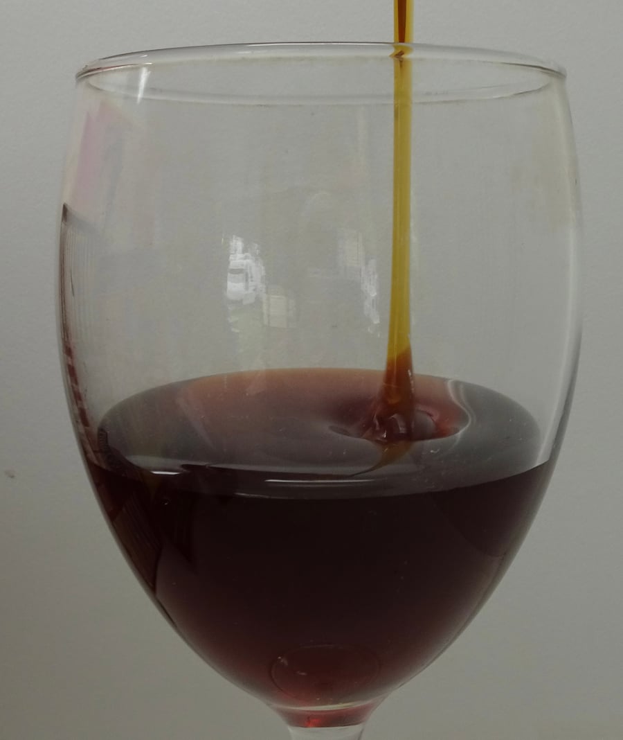 A wine glass half full of honey with a stream of honey pouring in.