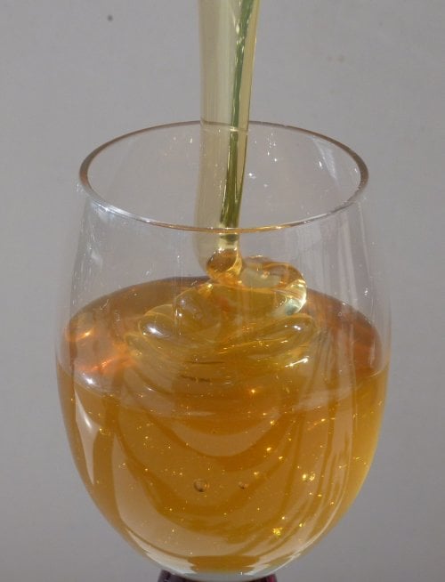 Pale golden linden honey pouring in a ribbon into a stemmed glass and coiling on the surface.