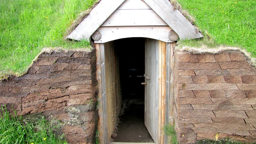 Wooden doorway with a peaked plank gable set into thick walls of stacked peat sods under grass.